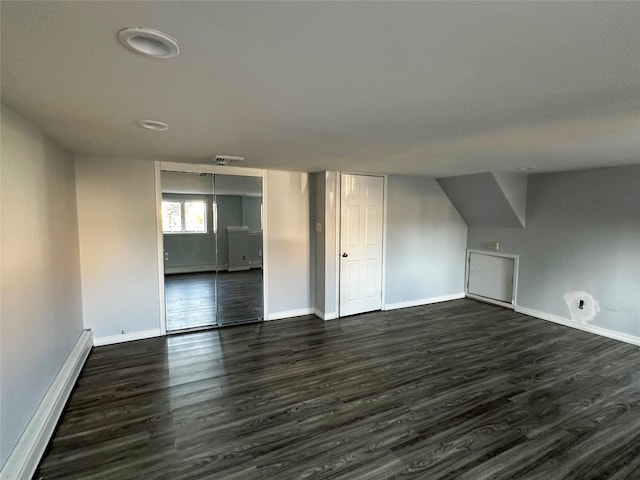 additional living space with a baseboard heating unit, baseboards, visible vents, and dark wood-style floors