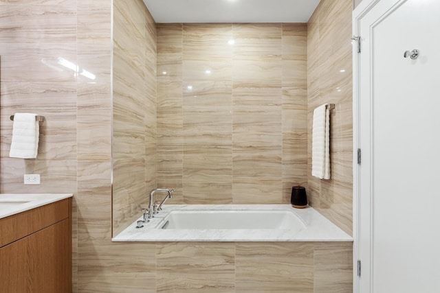 bathroom featuring tile walls, vanity, and tiled tub