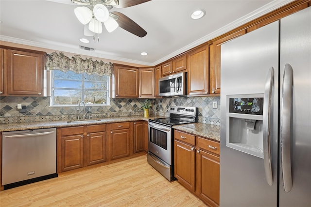 kitchen with light wood finished floors, visible vents, brown cabinetry, stainless steel appliances, and a sink