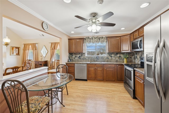 kitchen with a ceiling fan, a sink, light wood-style floors, appliances with stainless steel finishes, and crown molding