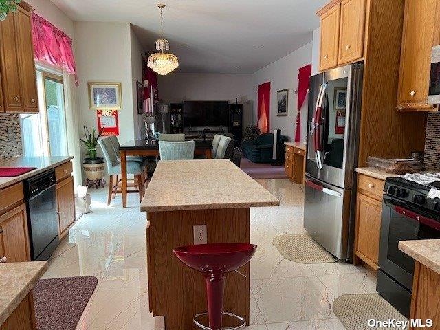 kitchen with decorative backsplash, black appliances, light countertops, pendant lighting, and open floor plan