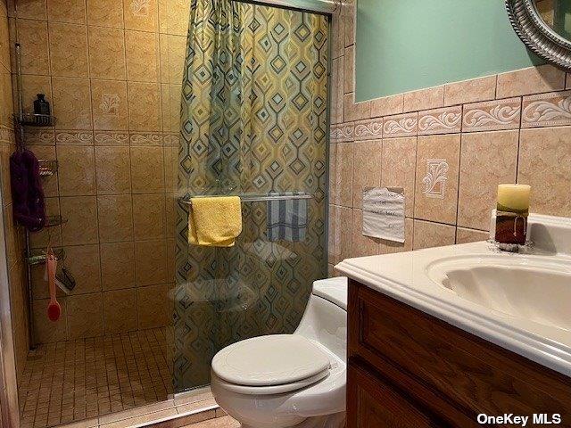 bathroom featuring a shower stall, vanity, toilet, and tile walls