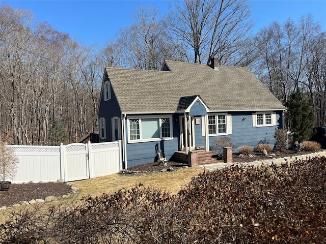 view of front facade featuring a chimney, a shingled roof, fence, and a gate