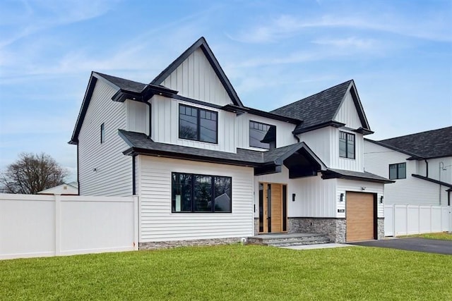 modern inspired farmhouse with fence, driveway, an attached garage, a front lawn, and board and batten siding