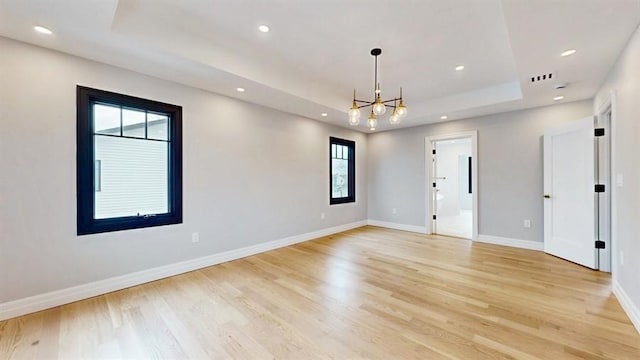 empty room featuring recessed lighting, baseboards, a raised ceiling, and a notable chandelier