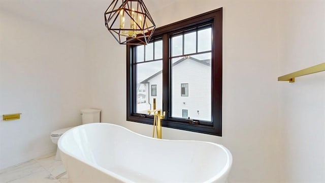 full bath with a notable chandelier, marble finish floor, and a freestanding tub