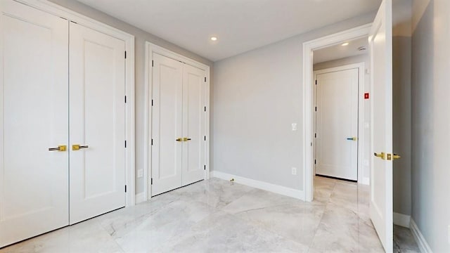 unfurnished bedroom featuring marble finish floor, baseboards, and two closets