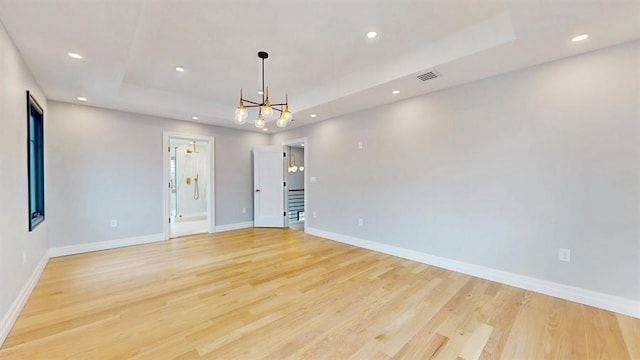 empty room with recessed lighting, a tray ceiling, baseboards, and light wood-style flooring