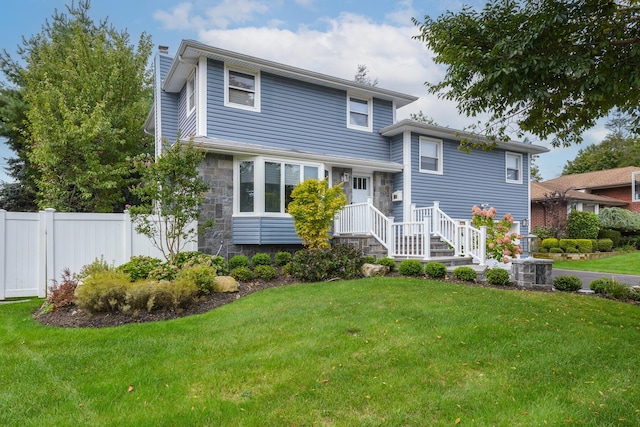 split level home with stone siding, a front lawn, a chimney, and fence