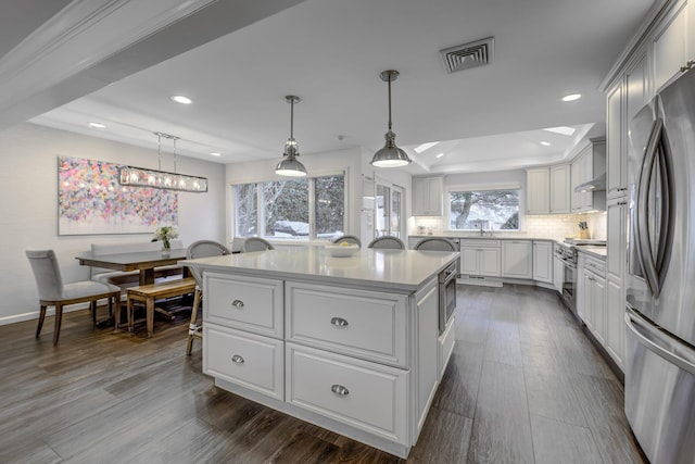 kitchen featuring visible vents, stainless steel appliances, decorative backsplash, light countertops, and a center island