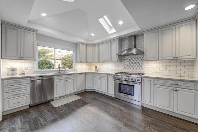 kitchen featuring light countertops, wall chimney exhaust hood, appliances with stainless steel finishes, and a sink