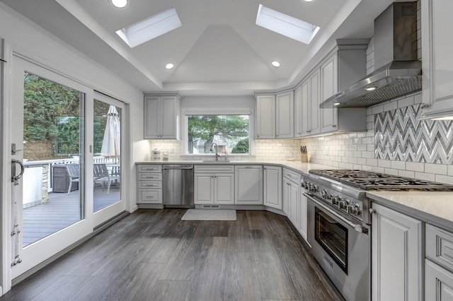 kitchen with a sink, wall chimney range hood, vaulted ceiling with skylight, appliances with stainless steel finishes, and light countertops