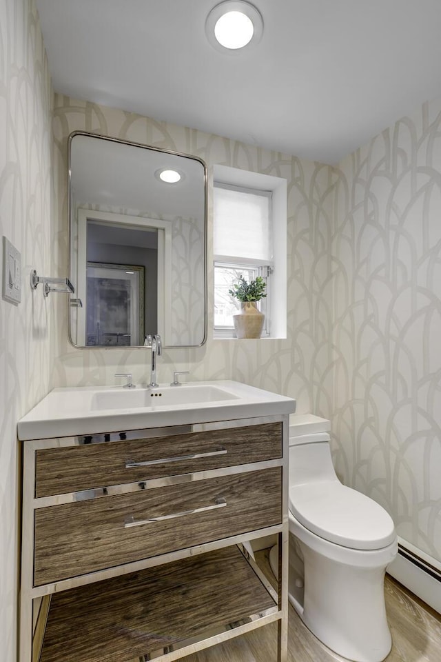 bathroom with toilet, vanity, wallpapered walls, and a baseboard heating unit