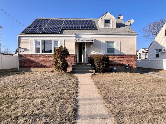 view of front of property with brick siding, solar panels, a shingled roof, and fence