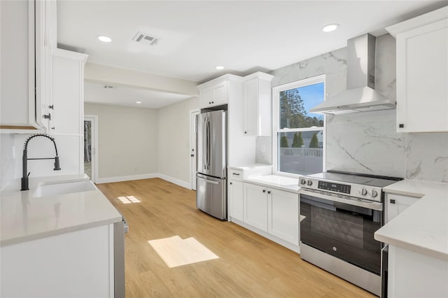 kitchen featuring a sink, white cabinetry, appliances with stainless steel finishes, and wall chimney range hood