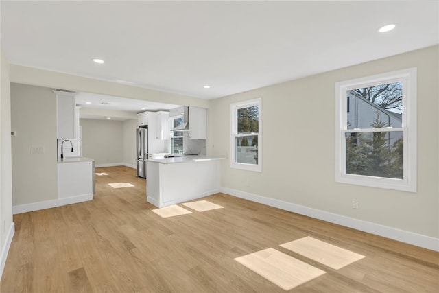 unfurnished living room with light wood finished floors, recessed lighting, baseboards, and a sink