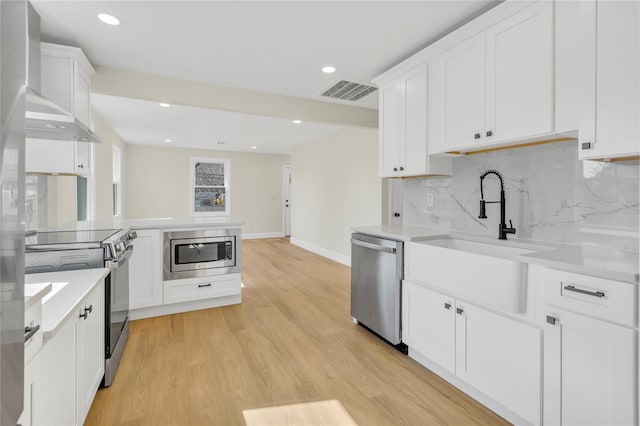 kitchen with visible vents, a sink, stainless steel appliances, light countertops, and wall chimney range hood