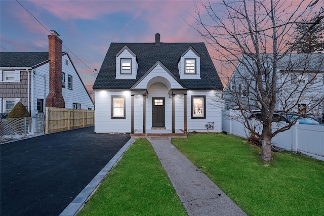 view of front facade with a lawn, a shingled roof, driveway, and fence