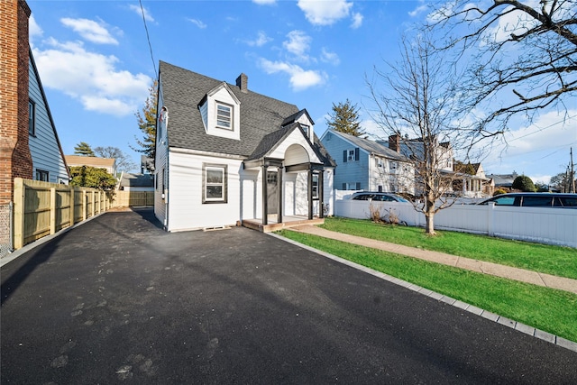 view of front facade with a front yard, fence private yard, a residential view, and roof with shingles