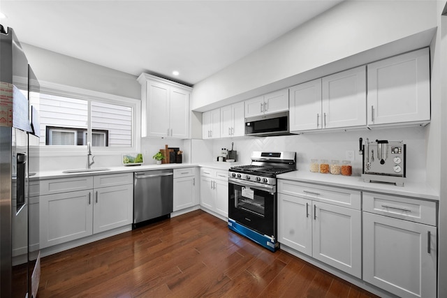 kitchen with dark wood-type flooring, a sink, white cabinetry, stainless steel appliances, and light countertops