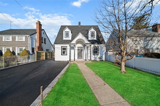 view of front of property with fence private yard, a front yard, roof with shingles, a chimney, and driveway