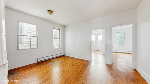 empty room with baseboard heating, a healthy amount of sunlight, a baseboard heating unit, and wood finished floors