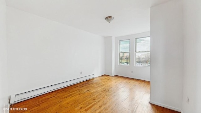 unfurnished room featuring baseboard heating, light wood-style flooring, and baseboards