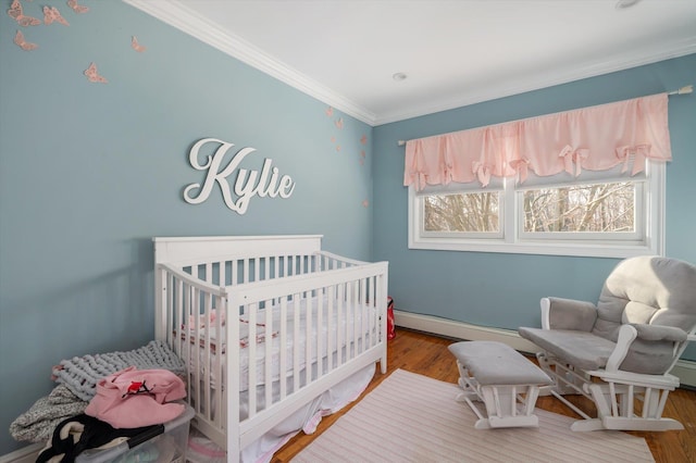 bedroom featuring a baseboard heating unit, a nursery area, wood finished floors, and crown molding