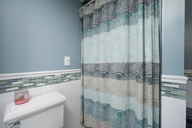 full bathroom with a wainscoted wall, curtained shower, toilet, and tile walls