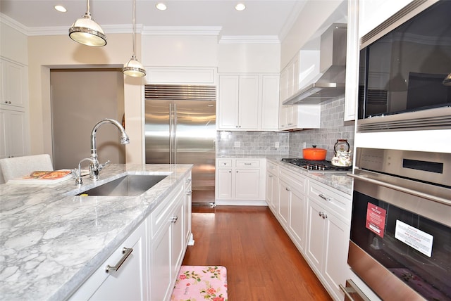 kitchen featuring crown molding, wall chimney range hood, appliances with stainless steel finishes, and a sink