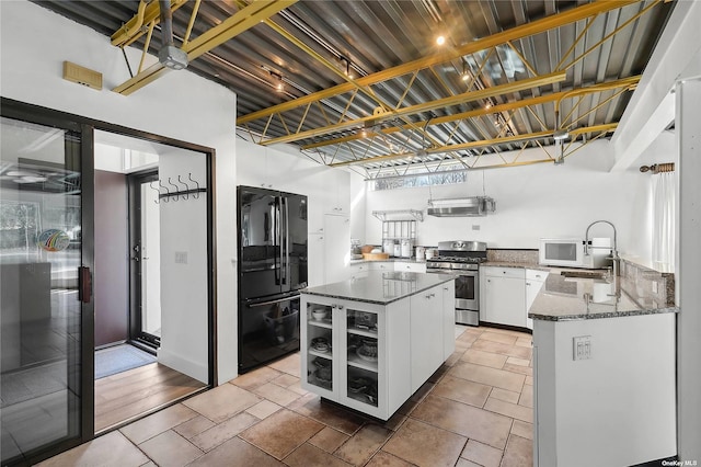 kitchen with a sink, dark stone countertops, freestanding refrigerator, white cabinets, and stainless steel gas range