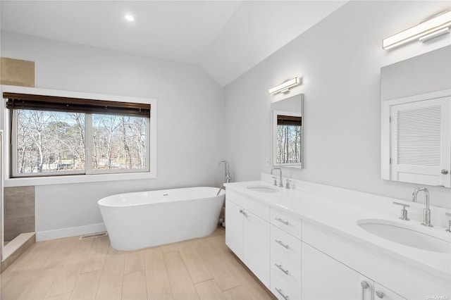 full bath with a sink, lofted ceiling, a soaking tub, and double vanity