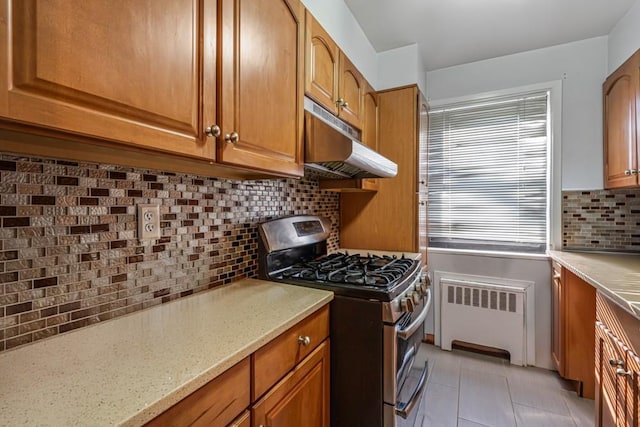 kitchen featuring brown cabinets, under cabinet range hood, gas stove, radiator, and light tile patterned flooring