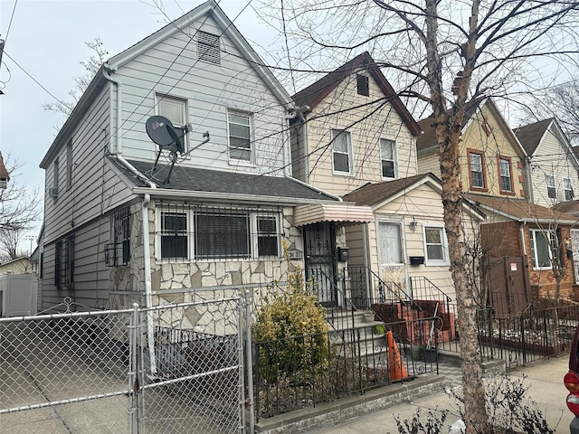 view of front of house featuring a fenced front yard, stone siding, a shingled roof, and a gate