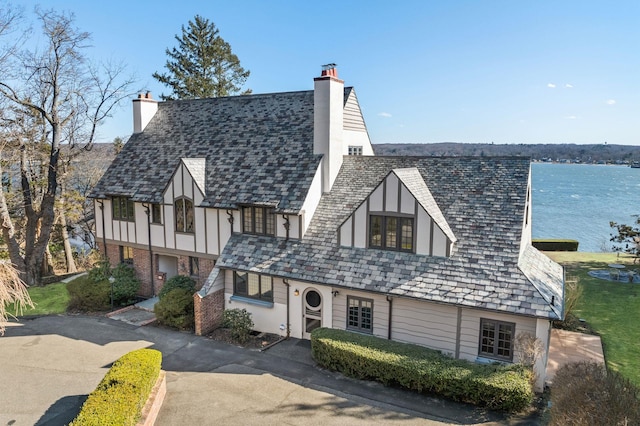 tudor-style house with stucco siding, a high end roof, and a chimney
