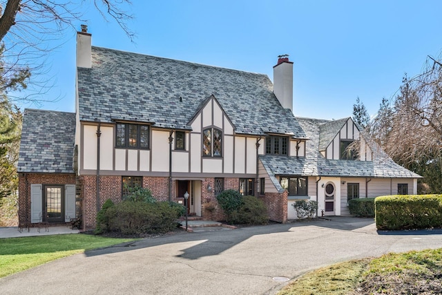 english style home featuring stucco siding, a high end roof, brick siding, and a chimney