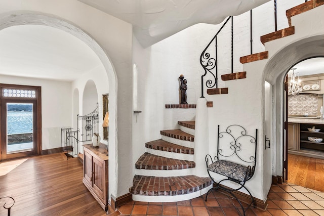 stairs featuring an inviting chandelier, wood finished floors, and arched walkways