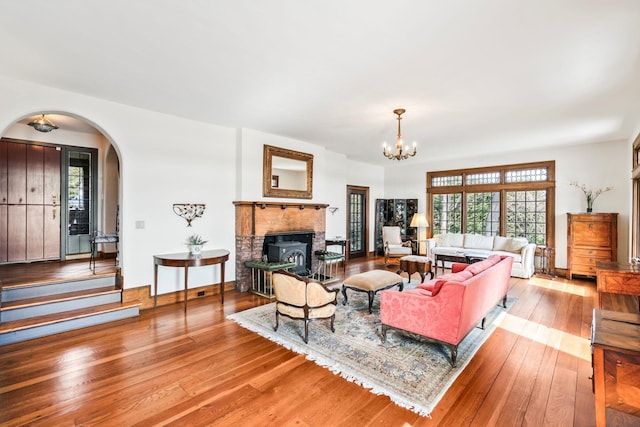 living room featuring baseboards, a fireplace, hardwood / wood-style flooring, arched walkways, and a notable chandelier