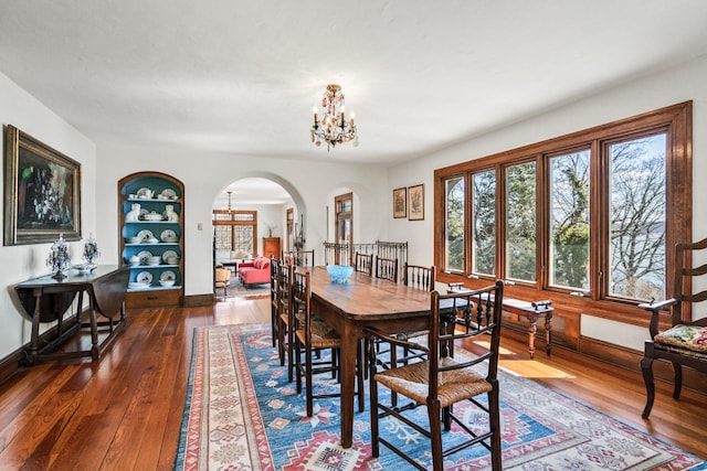 dining space with dark wood finished floors, a notable chandelier, baseboards, and arched walkways