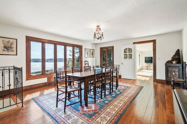 dining room featuring baseboards, a water view, a notable chandelier, and hardwood / wood-style flooring