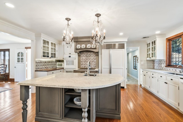 kitchen featuring white appliances, a center island with sink, light wood finished floors, a sink, and a chandelier