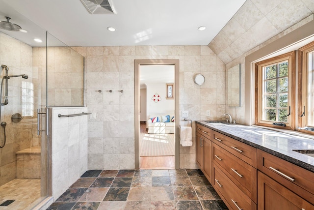 ensuite bathroom featuring visible vents, connected bathroom, vanity, a tile shower, and tile walls