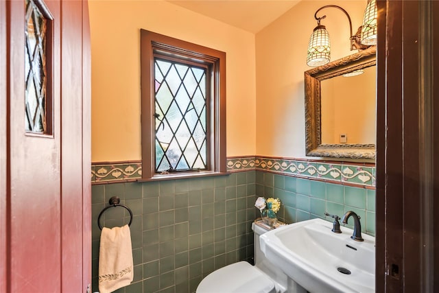 half bathroom with wainscoting, a healthy amount of sunlight, toilet, and a sink