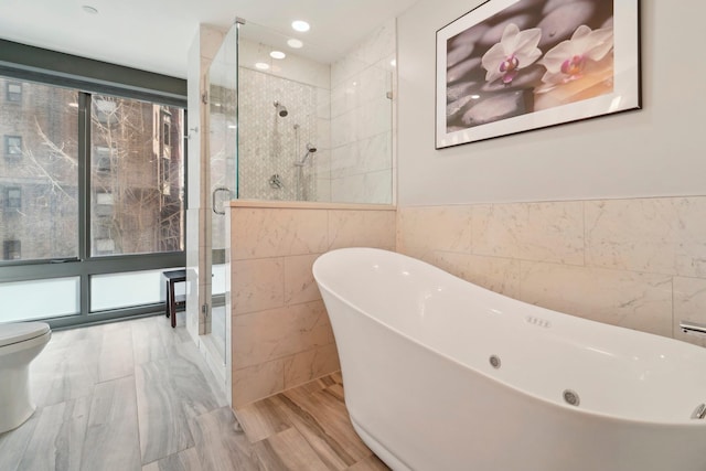 full bath with a freestanding bath, recessed lighting, a stall shower, wood finished floors, and tile walls