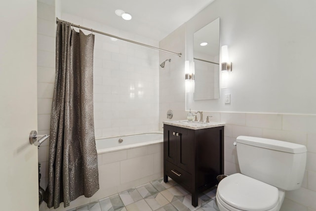 bathroom with toilet, vanity, wainscoting, tiled shower / bath combo, and tile walls