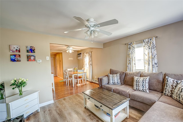 living room with light wood-style flooring, a wall unit AC, a ceiling fan, baseboard heating, and baseboards