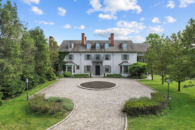 view of front of home featuring stucco siding, a chimney, a front yard, and curved driveway