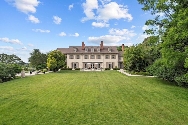 rear view of house featuring a patio area, a lawn, a chimney, and stucco siding