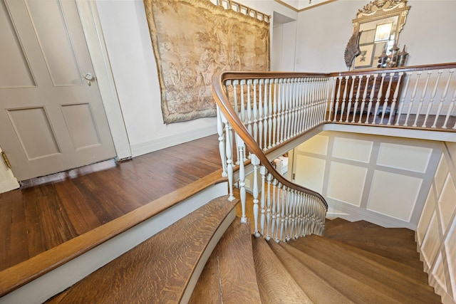 staircase featuring a decorative wall, baseboards, and wood finished floors