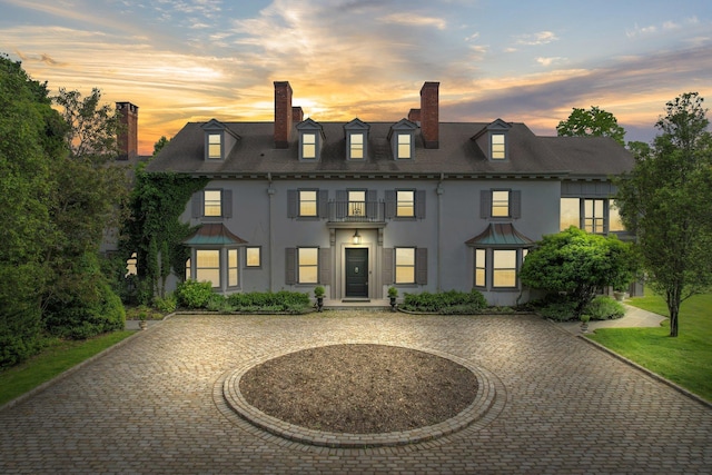 view of front of property featuring stucco siding, curved driveway, and a chimney